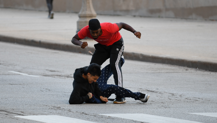 Hispanic man on ground, getting punched in the head by the Black guy in a red shirt.